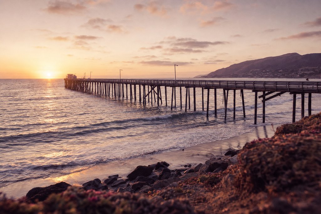 A long wooden pier over calm ocean at sunrise on the southern Californian coast. (AI-generated image)