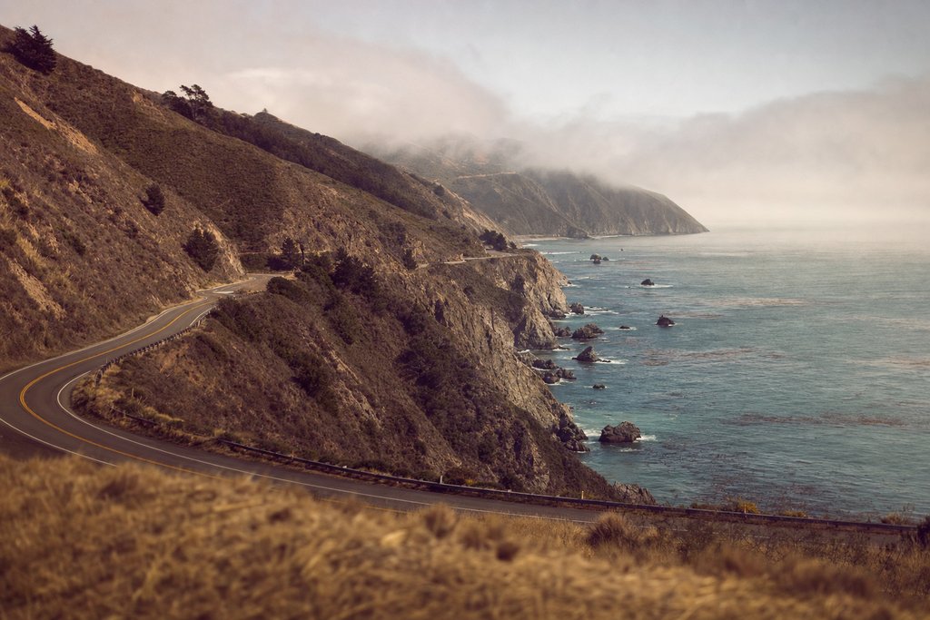 A two-lane highway on a cliff above the Pacific with a concrete arch bridge ahead. (AI-generated image)