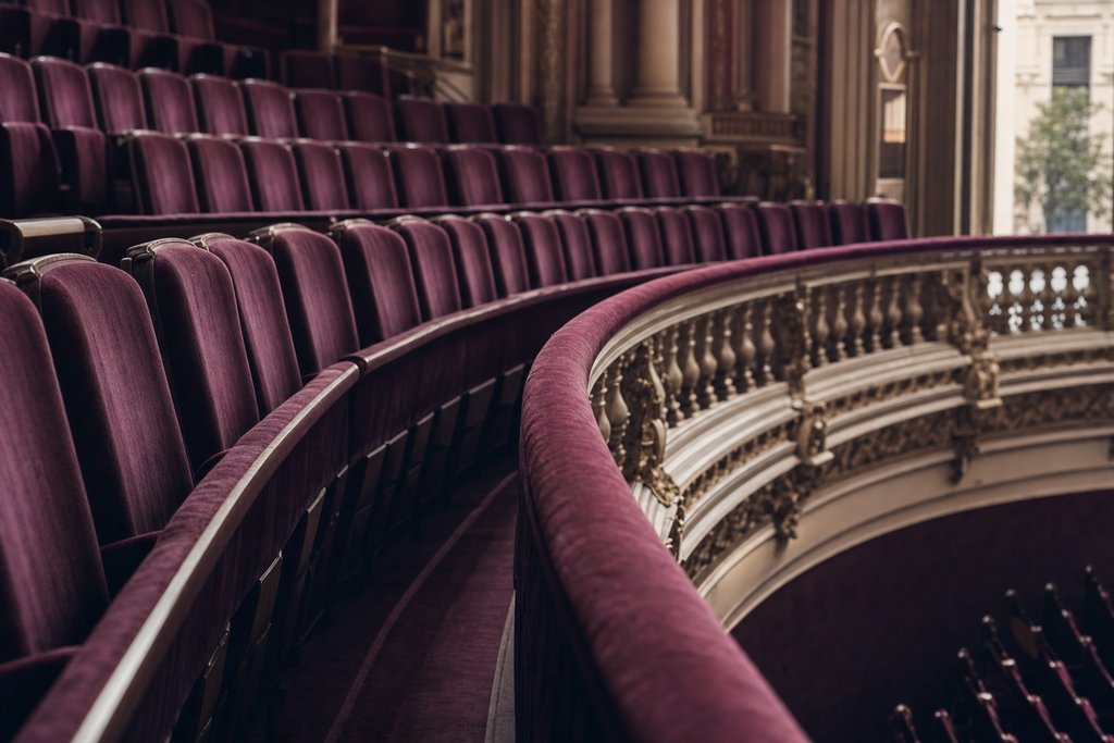 a curved cinema balcony rail above rows of empty upholstered seats. (AI-generated image)