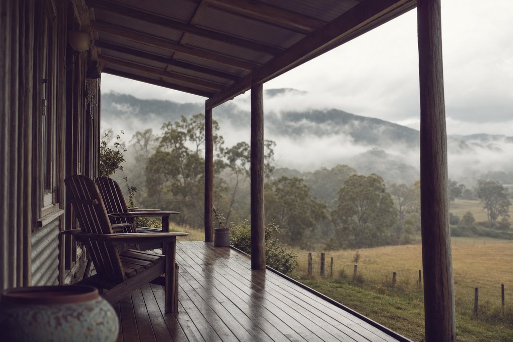 a tin-roofed cabin porch with two chairs looking out over a misty paddock. (AI-generated image)