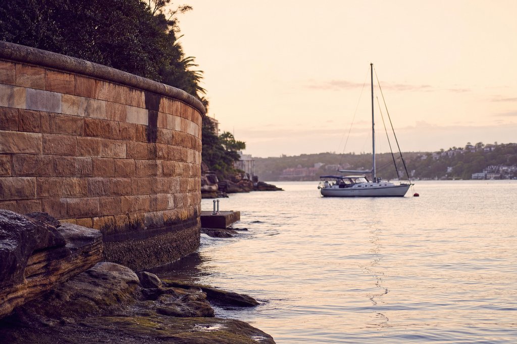 a sandstone sea wall and harbour water with a moored yacht at first light. (AI-generated image)