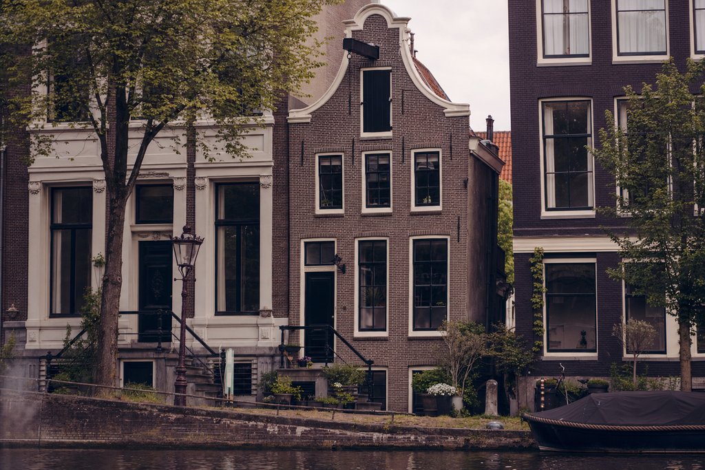 a narrow brick canal house front with a hoisting beam and a black door. (AI-generated image)