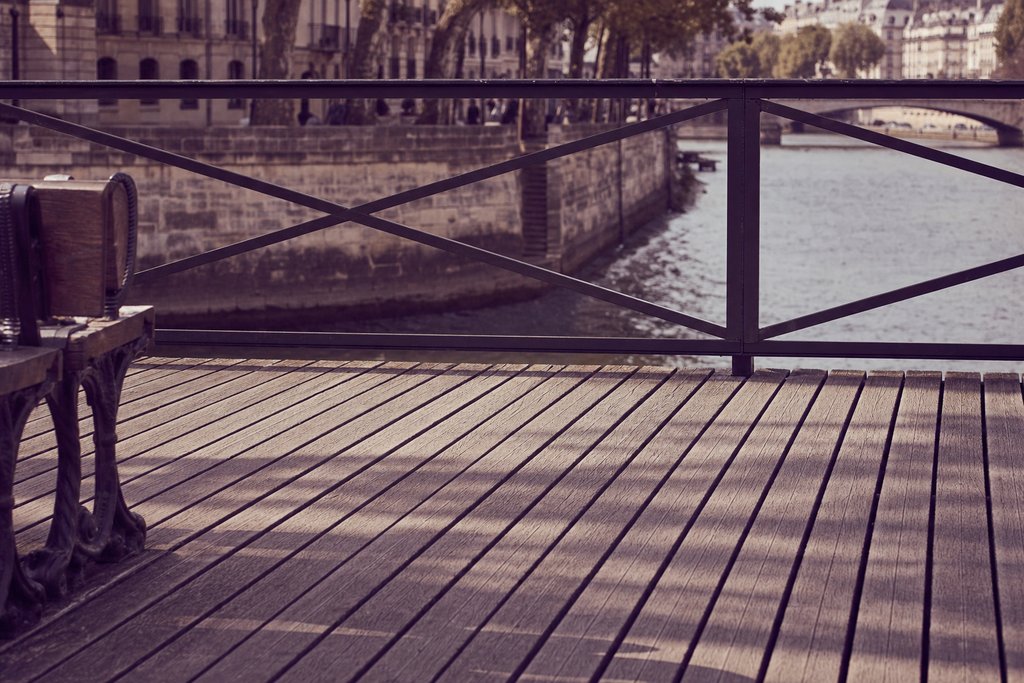 a pedestrian bridge deck of timber planks with a river and stone quay beyond. (AI-generated image)