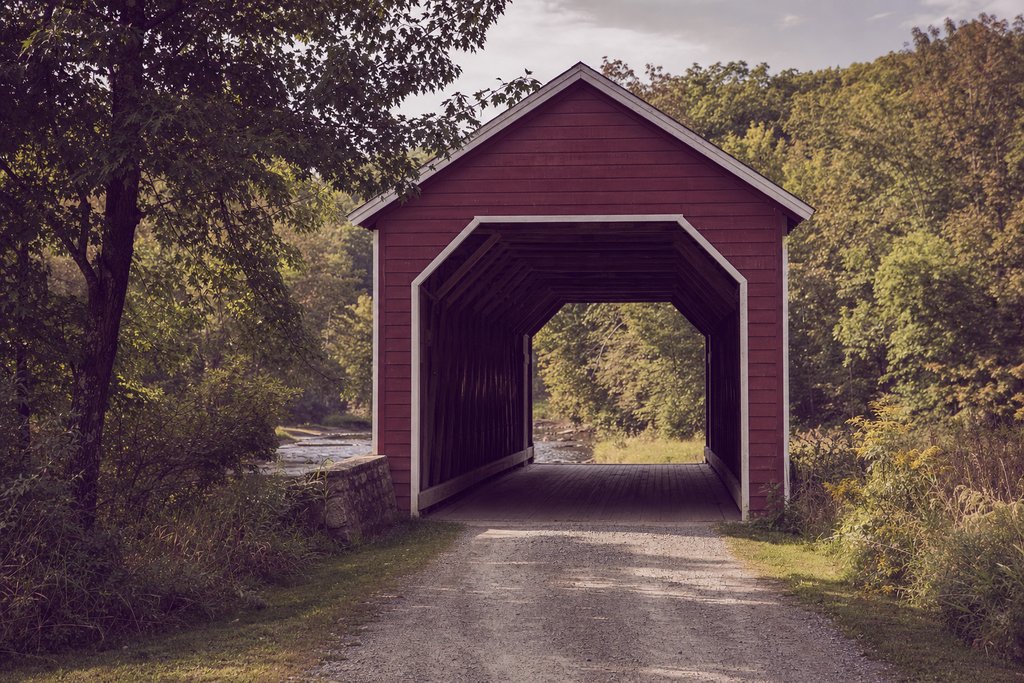 a red timber covered bridge portal seen from a gravel track in late summer. (AI-generated image)