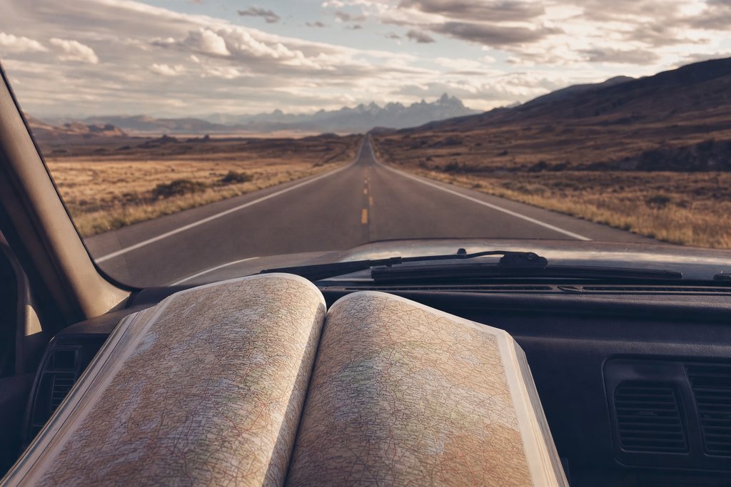 an open road atlas on a car dashboard with an empty road beyond the windscreen. (AI-generated image)