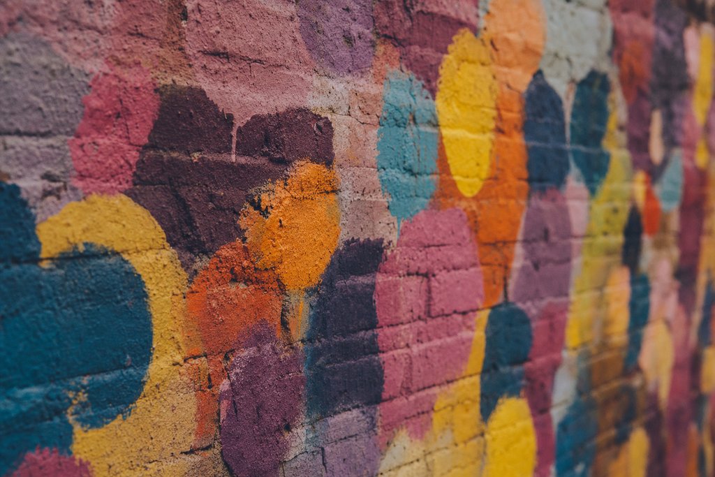 a close view of a brick wall dense with overlapping blobs of bright colour, shallow focus. (AI-generated image)