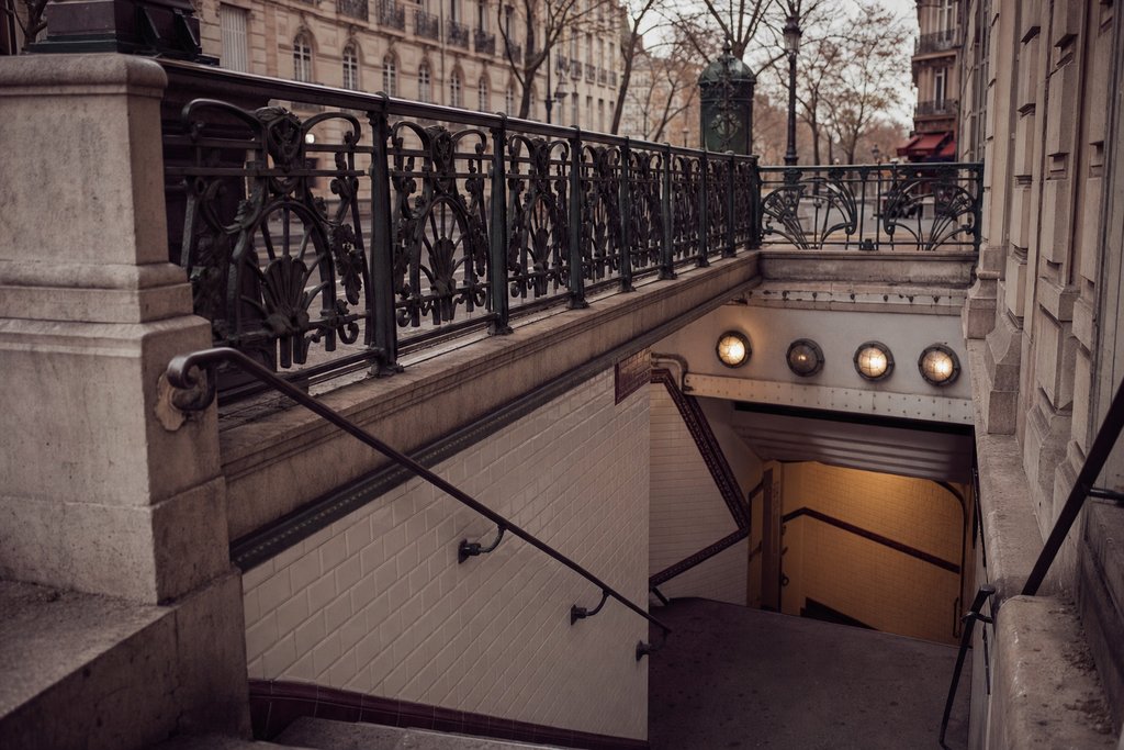 a tiled European metro entrance with a wrought-iron balustrade and steps down. (AI-generated image)