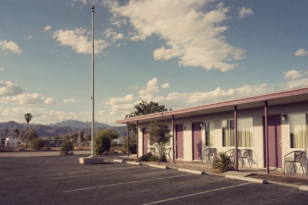 an empty motel car park with a low block and a bare flagpole under wide sky. (AI-generated image)