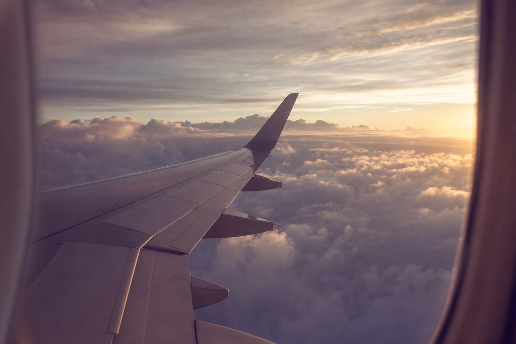 a window seat view over an aircraft wing above cloud in late afternoon. (AI-generated image)
