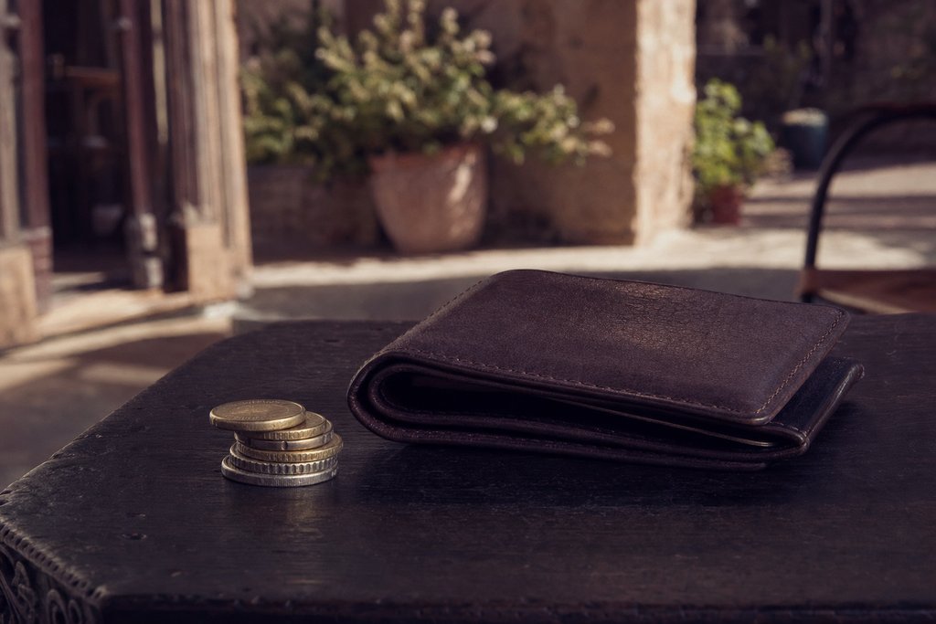 a folded leather bill holder and a small stack of coins on a dark table. (AI-generated image)