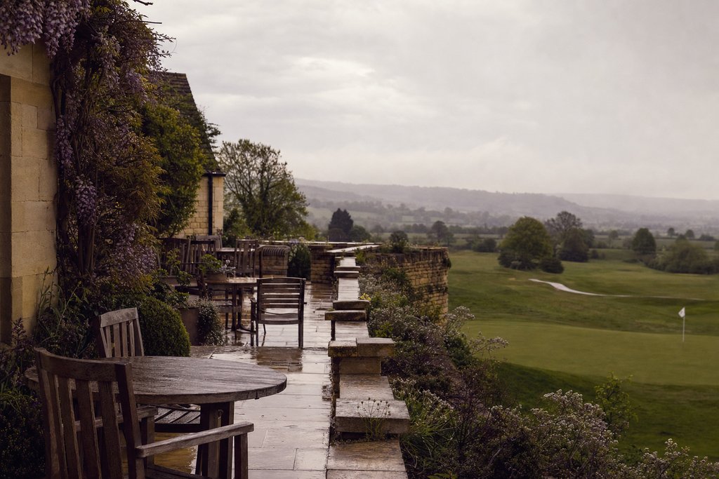 a honey-limestone terrace above a sloping green in soft English drizzle. (AI-generated image)