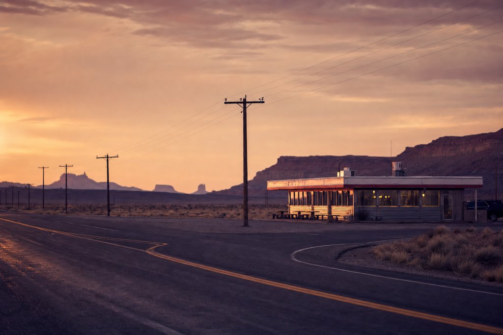 a neon-free American highway junction with a lone diner and telegraph poles at dusk. (AI-generated image)