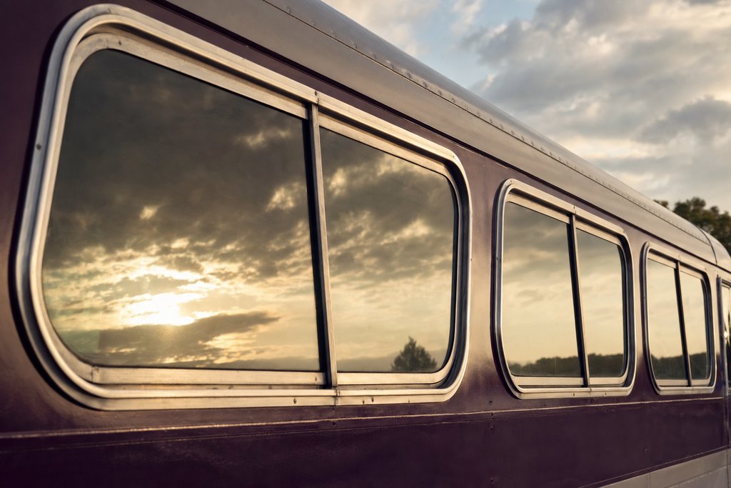a row of chrome-framed bus windows reflecting a low Southern sky. (AI-generated image)