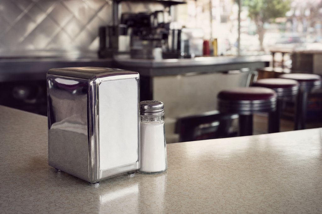 a chrome napkin dispenser and salt shaker on a formica diner counter. (AI-generated image)