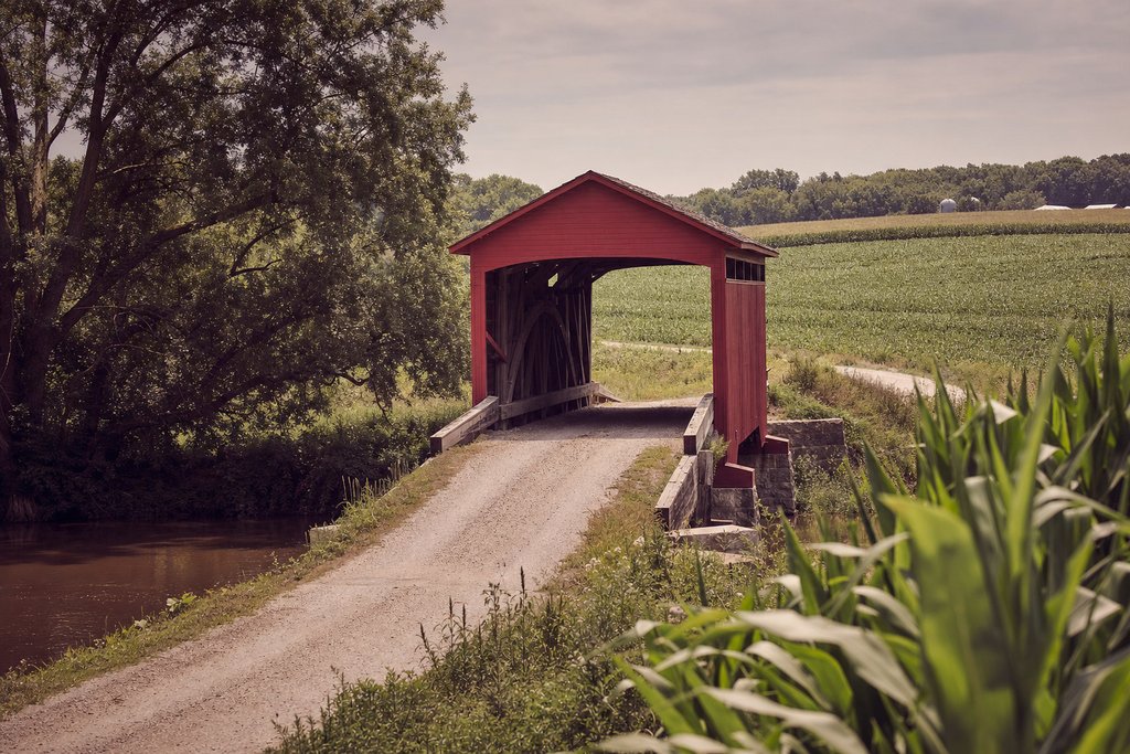 A timber covered bridge on stone abutments over a slow Iowa river in summer. (AI-generated image)