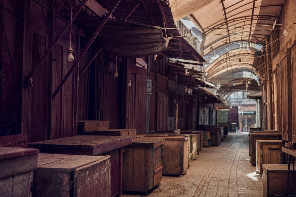 A covered market corridor of closed stalls early in the morning, timber counters and bare bulbs. (AI-generated image)