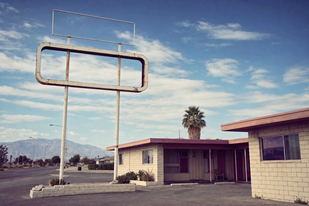 A blank roadside sign frame above a low block motel under a wide blue sky. (AI-generated image)