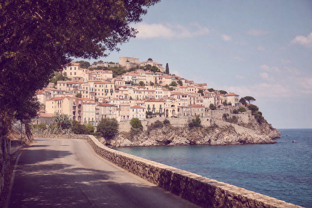A coastal town of pale render and terracotta roofs stacked up a headland above open water. (AI-generated image)