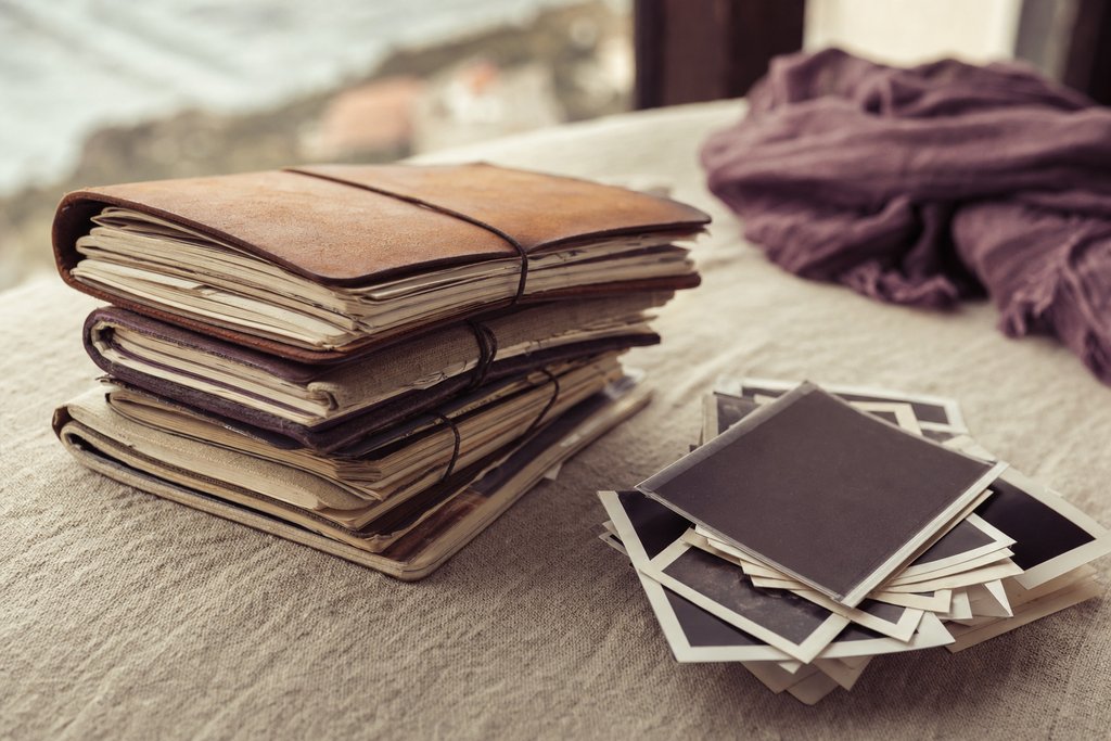 A stack of dated paper notebooks and a pen on a desk beside a window. (AI-generated image)