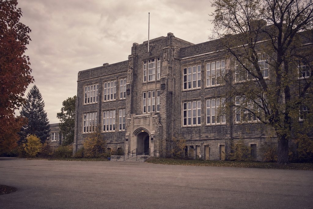A red brick school building with white sash windows above a mown quadrangle in spring. (AI-generated image)