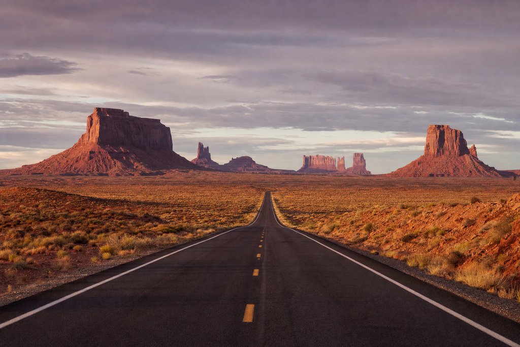 A red dirt road running straight toward tall sandstone buttes through dust haze. (AI-generated image)