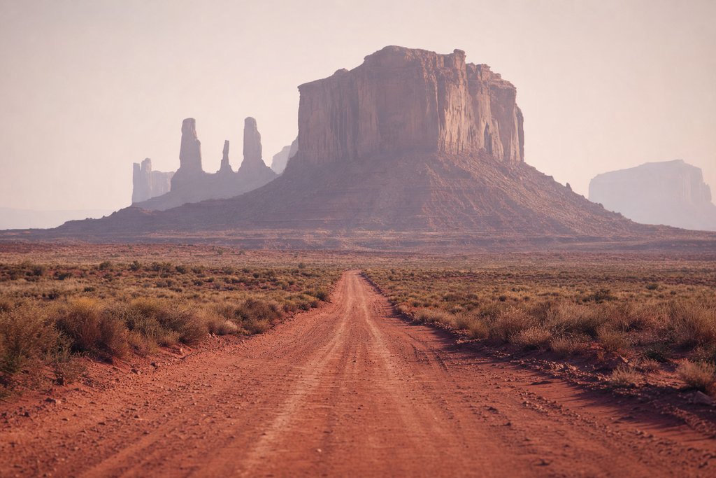 A red dirt road running straight toward tall sandstone buttes through dust haze. (AI-generated image)