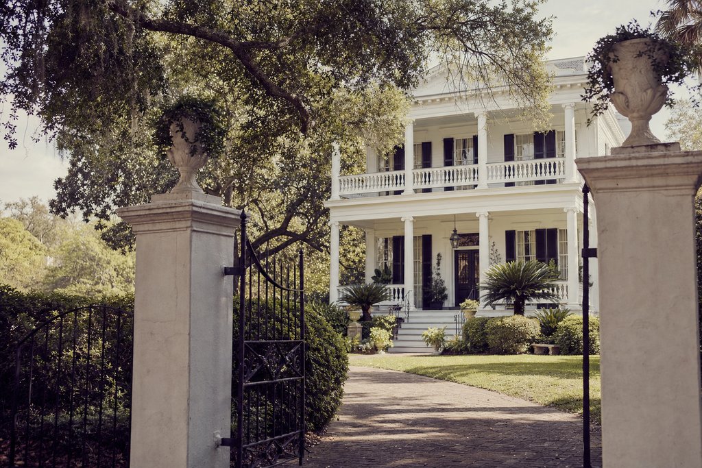 A two-storey antebellum house with white columns seen through an open iron gate, Carolina low country. (AI-generated image)