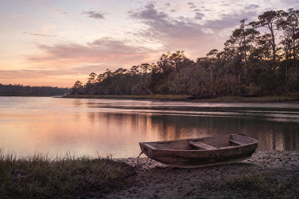 A wooden rowboat drawn up on the bank of a still blackwater lake ringed with cypress trees. (AI-generated image)