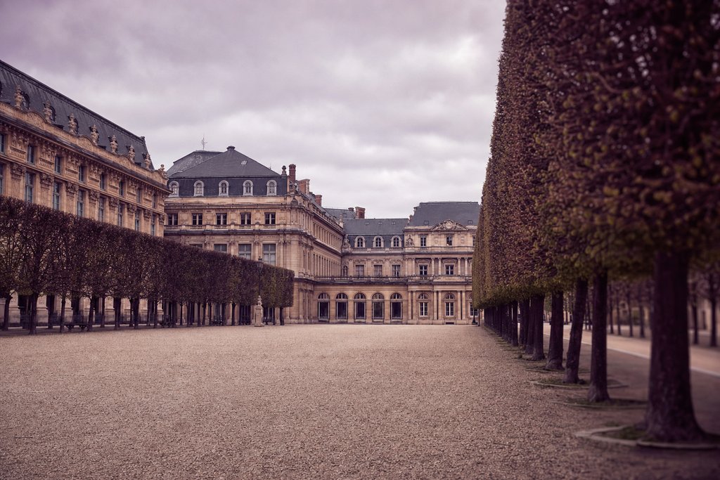 A large classical courtyard of gravel and clipped trees under overcast Paris light. (AI-generated image)