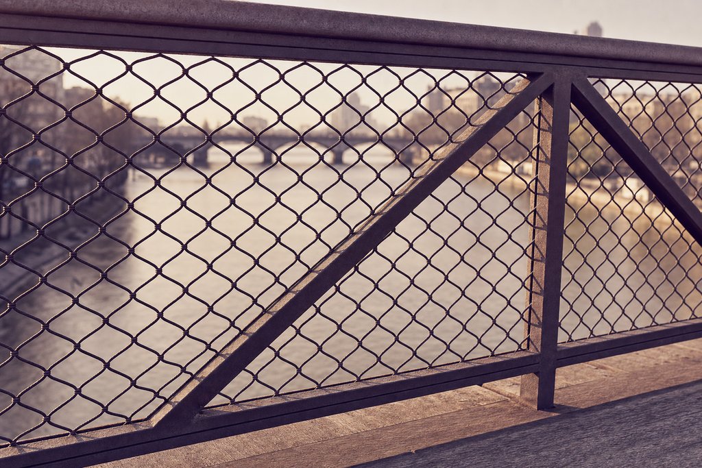 A close view of a bridge's steel mesh railing with the river beyond and nothing attached to it. (AI-generated image)