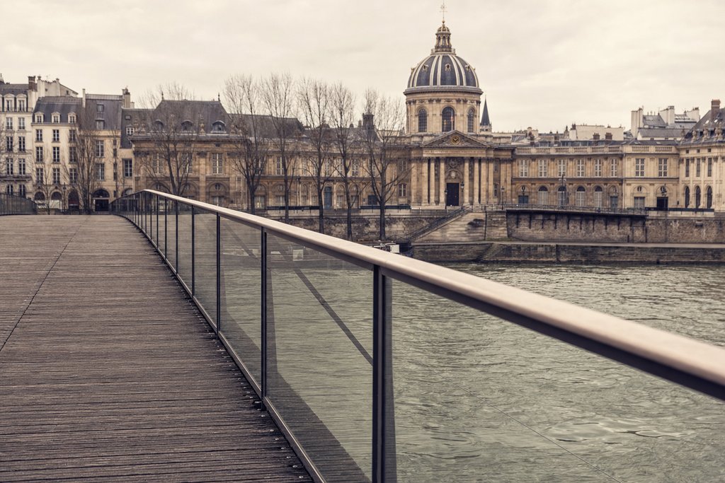 The Seine at dusk seen from a stone quay with a bridge arch and closed bookstalls above. (AI-generated image)