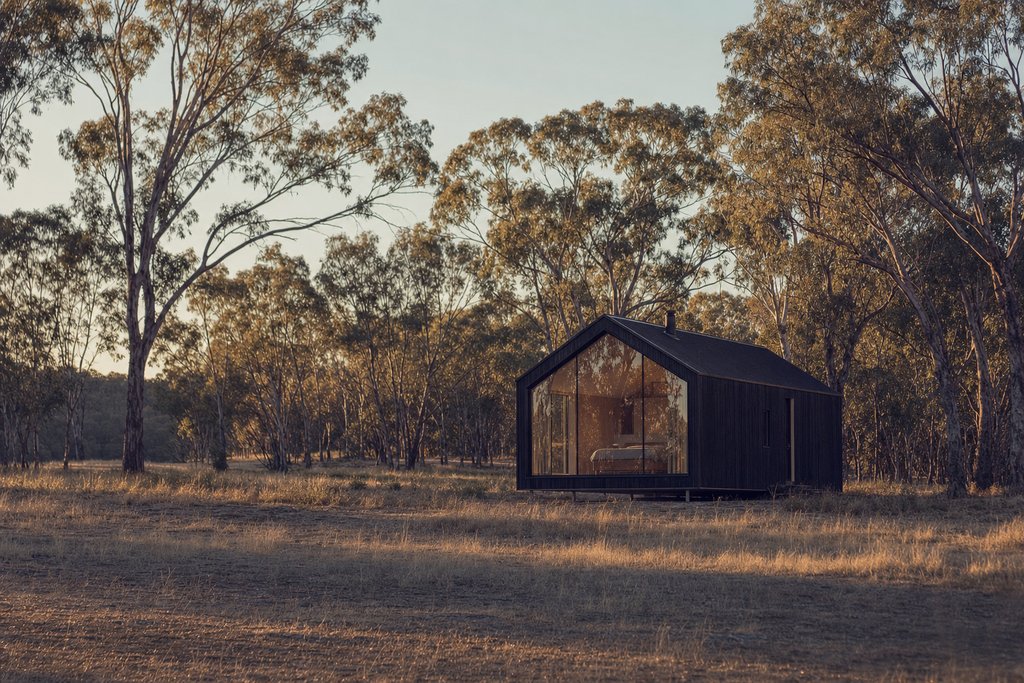A single small timber cabin alone in a green paddock ringed by gum trees in morning mist. (AI-generated image)