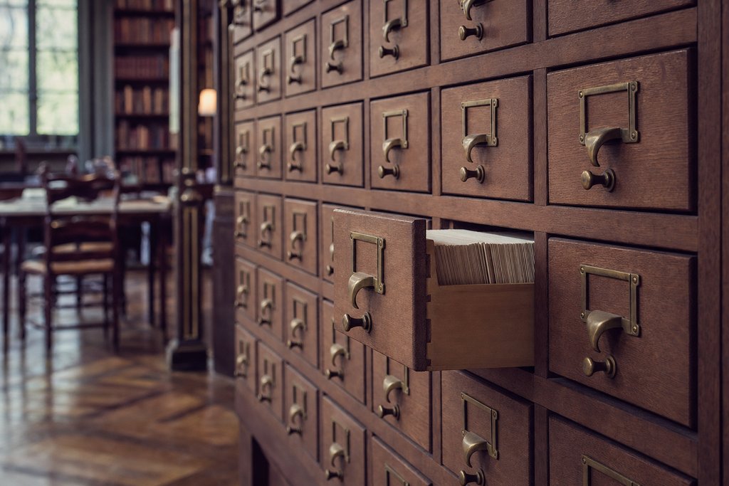 A wall of wooden library card-catalogue drawers with brass handles, one drawer pulled half open. (AI-generated image)
