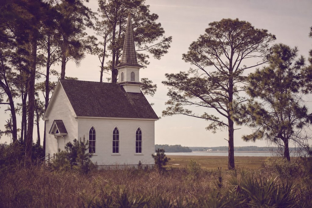 A small white weatherboard chapel with a shingled spire standing among pines on the coastal plain. (AI-generated image)