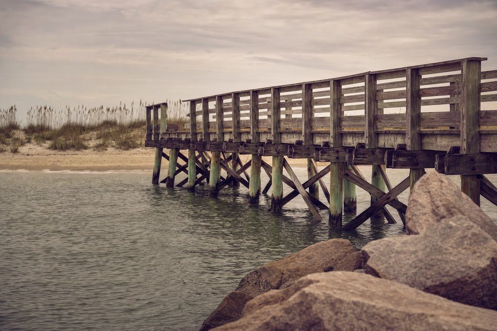 A long timber pier reaching out over calm Atlantic water at sunrise, North Carolina coast. (AI-generated image)