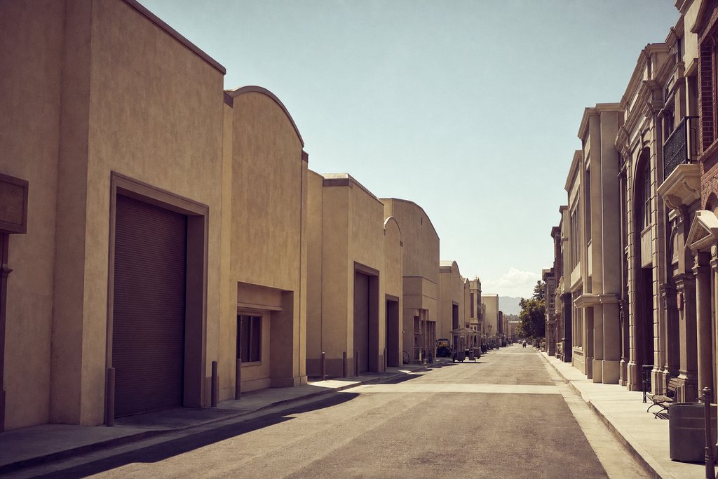 An empty backlot street of false-front American storefronts at midday, blank shopfronts. (AI-generated image)