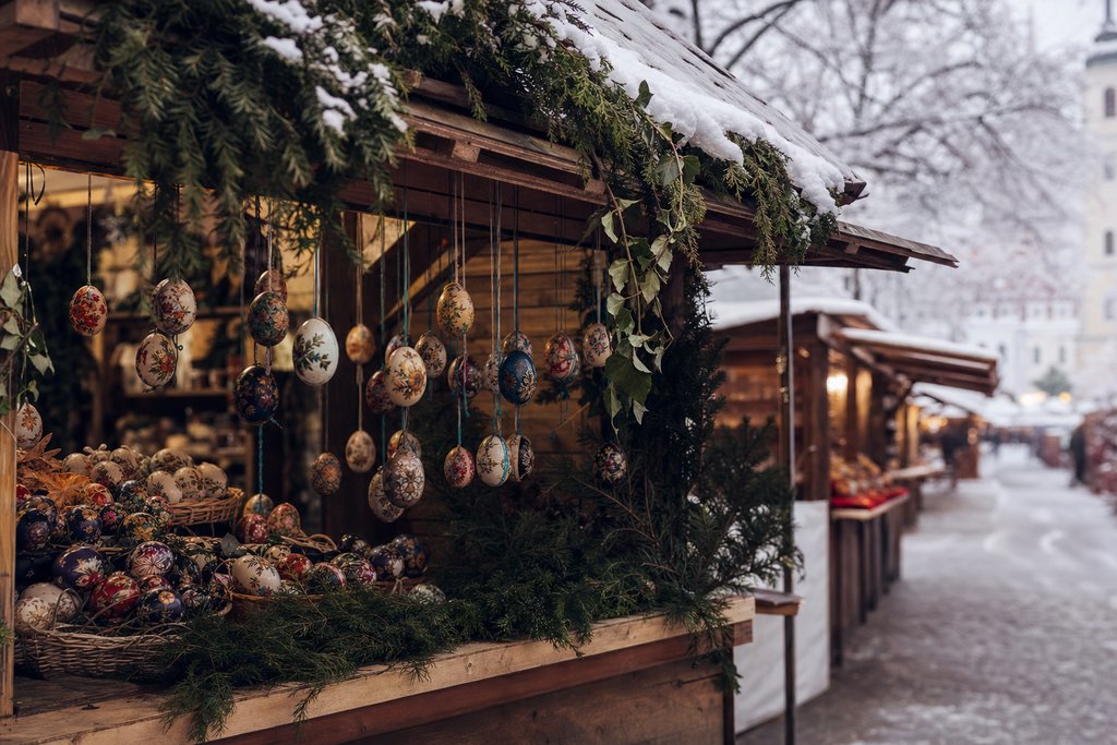 A wooden Christmas market stall of hand-painted eggs and greenery with snow on its roof. (AI-generated image)
