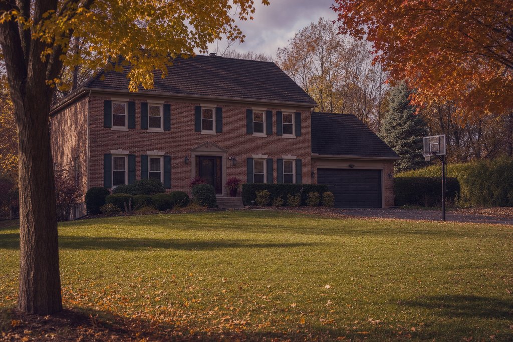 A two-storey brick suburban family house with a wide lawn and a basketball hoop, Illinois autumn. (AI-generated image)